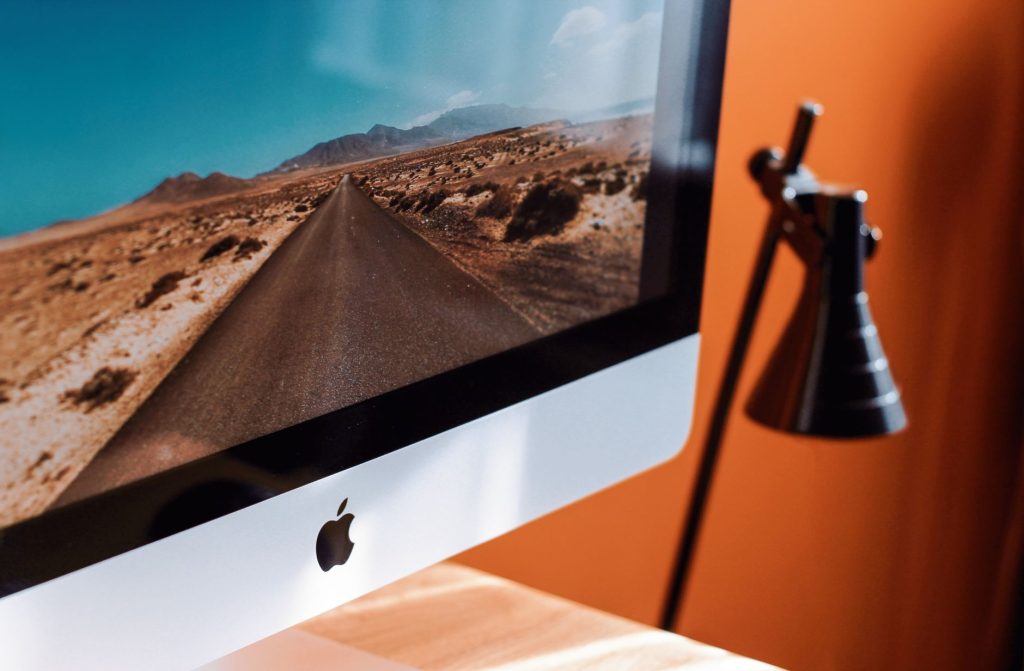 Як прискорити повільний комп’ютер: 7 робочих способів A sleek modern workspace featuring an iMac displaying a desert road and a stylish desk lamp.