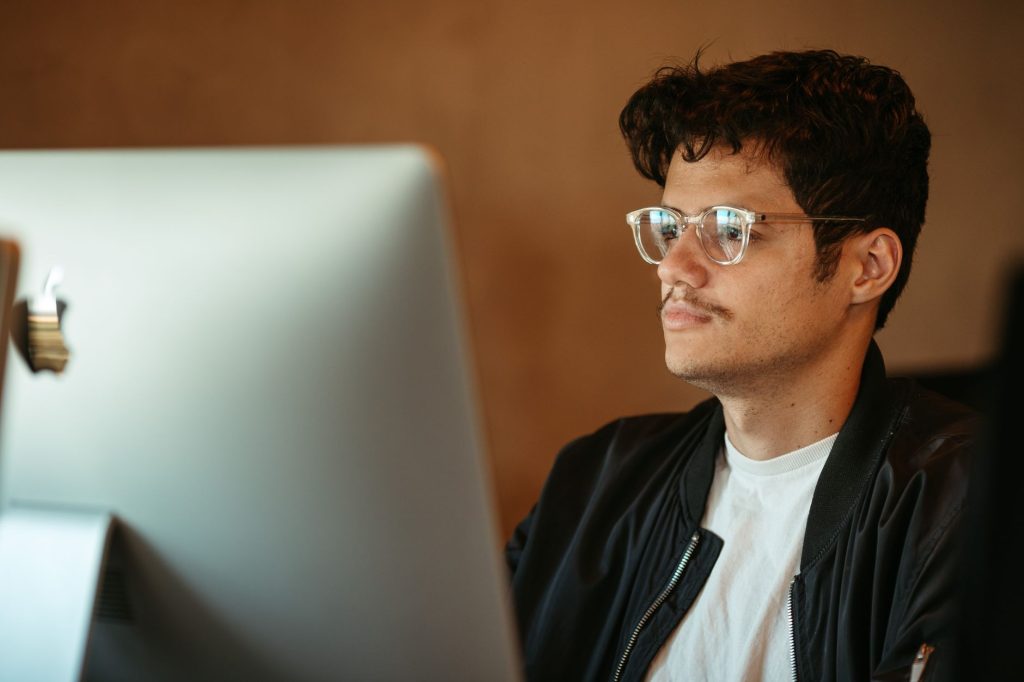 Здоров’я очей за комп’ютером: правила та звички Young man in eyeglasses focusing on computer screen indoors.