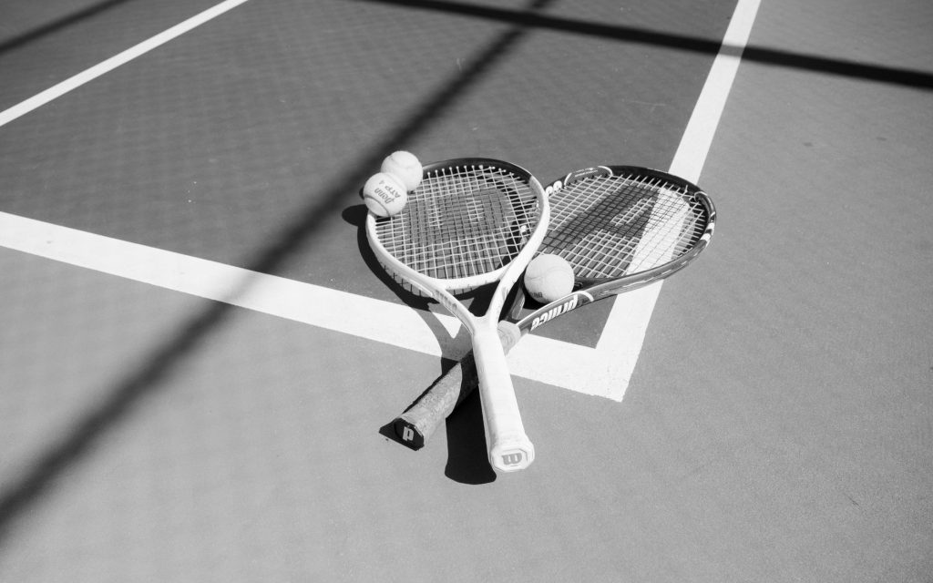 Як почати грати в теніс: гайд для початківців Monochrome image of two tennis rackets and balls on a sunlit court.