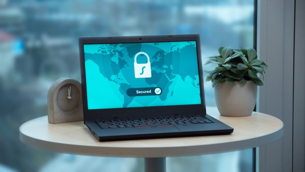 Що таке VPN і навіщо він потрібен звичайному користувачу Laptop displaying a security lock icon on a table with a potted plant and clock.