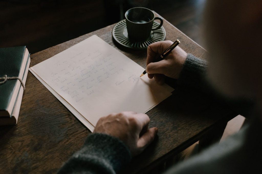 Правило двох хвилин: як перемогти прокрастинацію An adult writing a letter on a wooden desk with a cup of coffee, embodying a warm, intimate atmosphere.