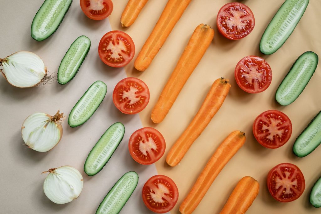 Продукти для імунітету: що їсти для міцного здоров’я Top view of fresh sliced vegetables including carrots, cucumbers, onions, and tomatoes in a flat lay design.