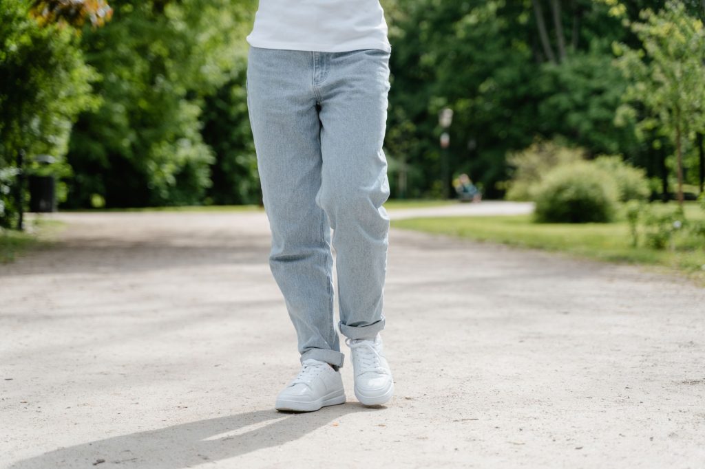 Ходьба для здоров’я: користь щоденних прогулянок A close-up view of a person walking on a park pathway wearing blue jeans and white sneakers.