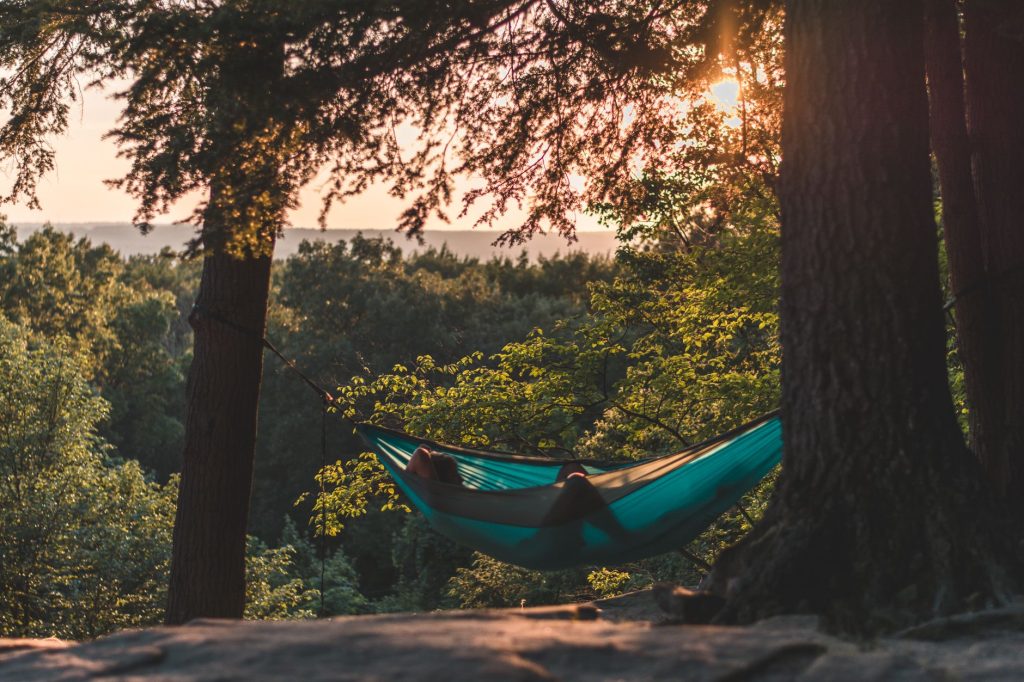 Мистецтво відпочинку: як відновлювати сили правильно Serene scene of a person relaxing in a hammock amidst a sunlit forest, capturing tranquility.