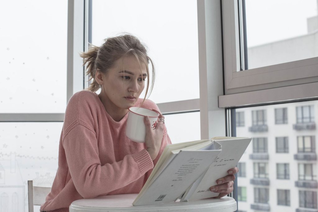 Як навчитися казати ні без почуття провини Casual woman enjoying a book with coffee by a bright window scene.