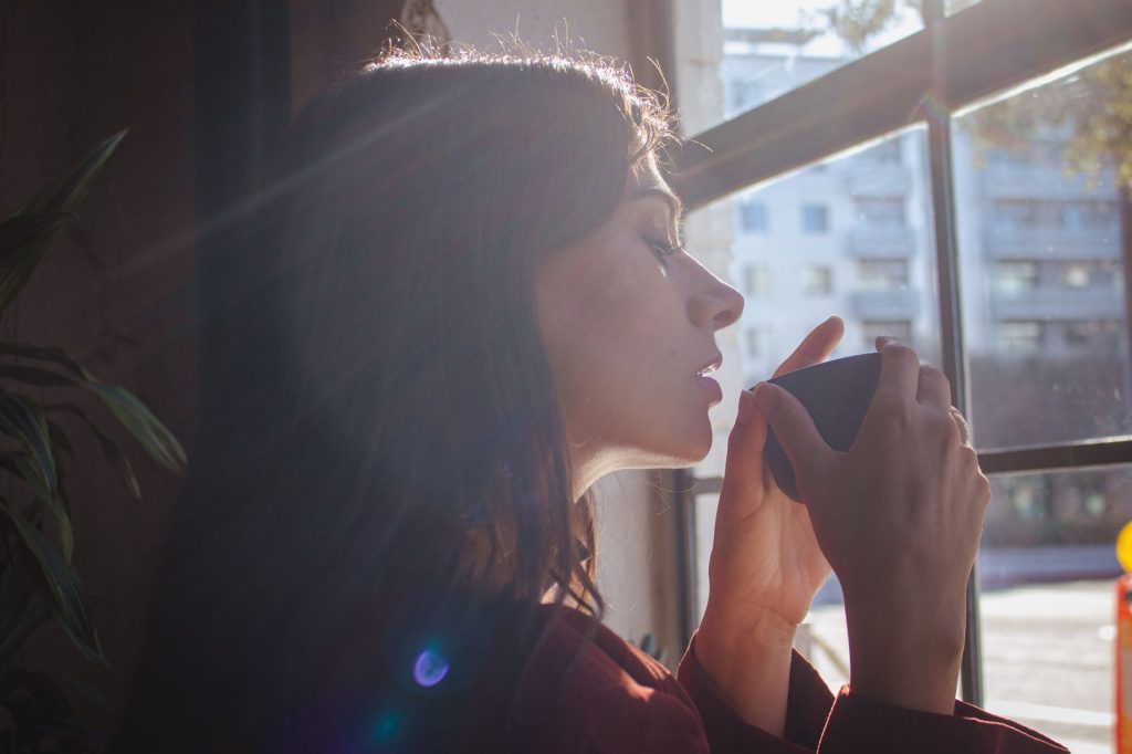 Ранкові ритуали, що задають тон усьому дню A woman savors a hot drink by a sunlit window in an urban setting.
