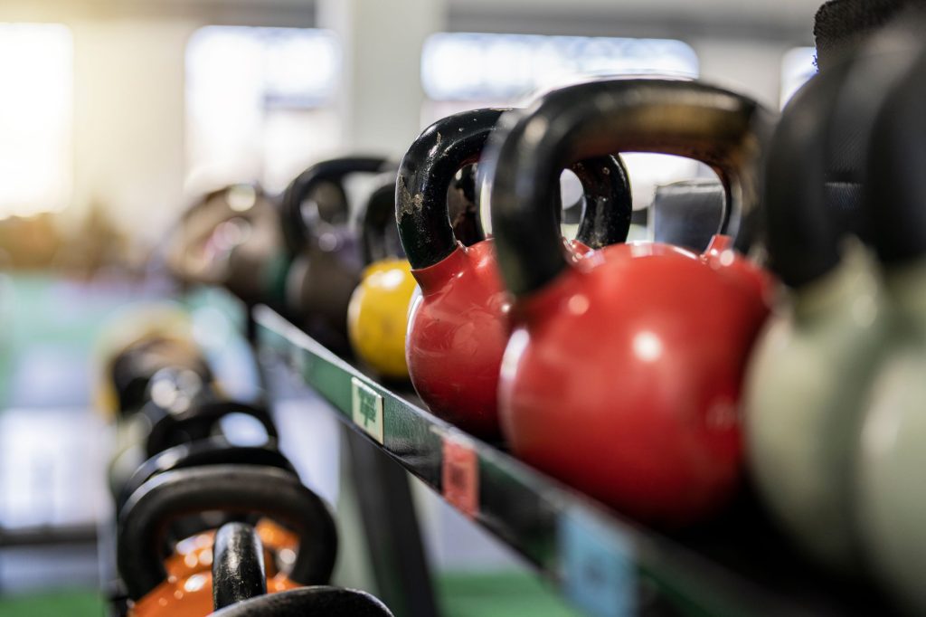 Тренування з гирею для початківців: базові вправи Close-up of colorful kettlebells on a rack in a modern gym indoors.