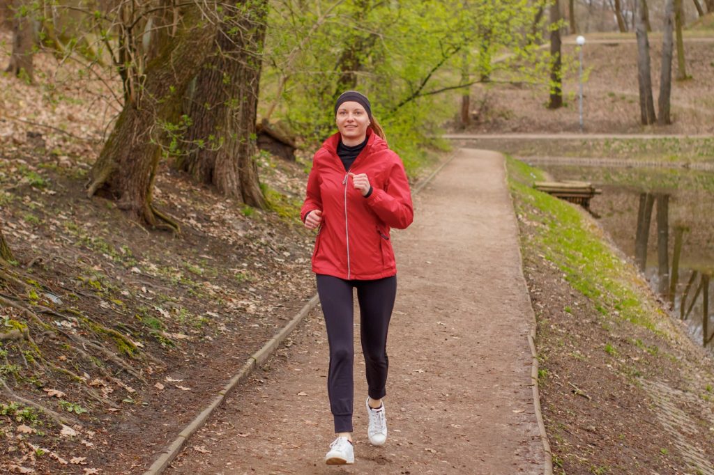 Woman in a red jacket jogging on a forest footpath during springtime.