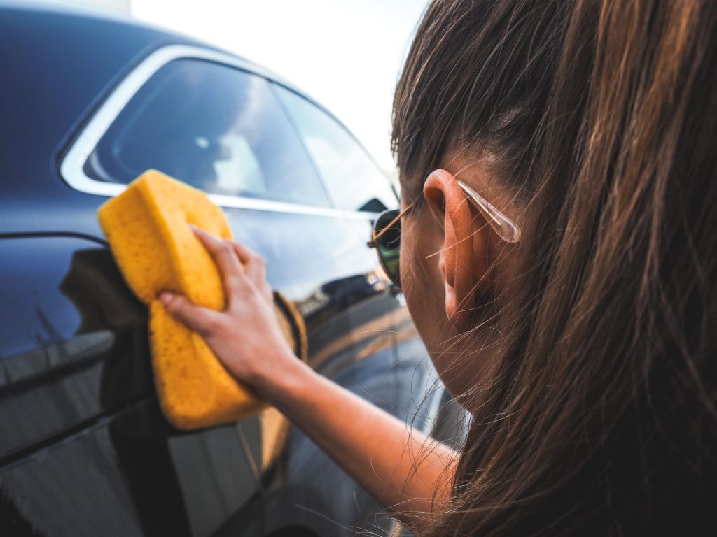 Догляд за кузовом авто: як зберегти фарбу надовго Close-up of a woman handwashing a black car using a yellow sponge, highlighting cleaning process.