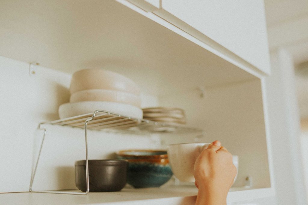 Розхламлення дому: з чого почати, щоб не закинути A person reaches into a kitchen cabinet to grab a mug, surrounded by neatly stacked dishes.