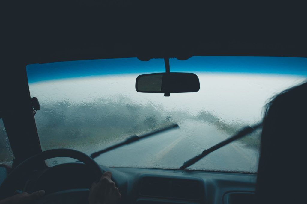 Щітки склоочисника: як вибрати та доглядати за ними Interior car view on a rainy day with water droplets on windshield and wipers in motion.