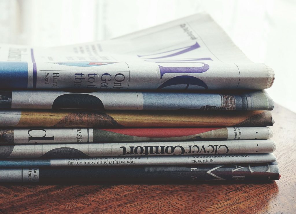 Як відрізнити фейкові новини від сатири: розбираємось A stack of folded newspapers placed on a wooden table, symbolizing news and information.