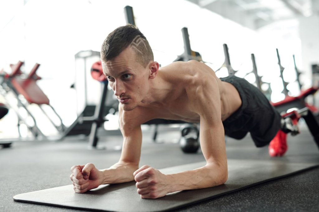 Планка: як правильно робити й що дає ця вправа тілу A shirtless man with a prosthetic leg planks on a yoga mat in a gym, showcasing fitness and determination.