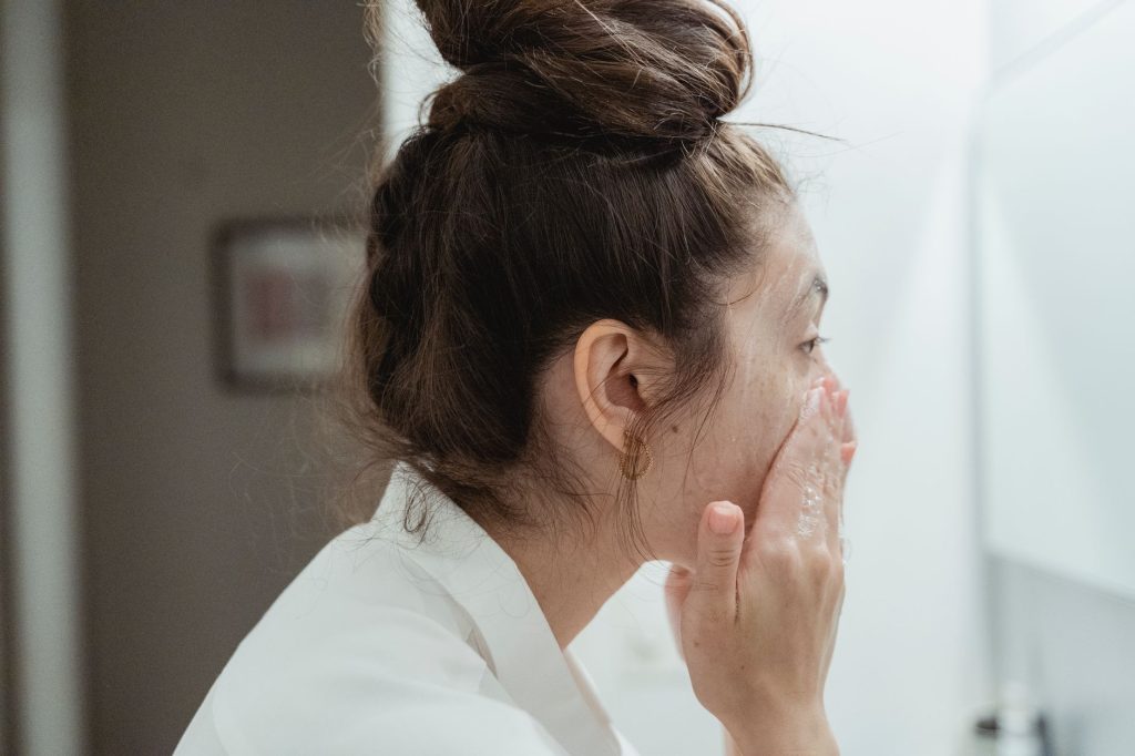 Догляд за шкірою обличчя за типом: повний гід A young woman in a bathrobe follows her skincare routine, washing her face in a bathroom.