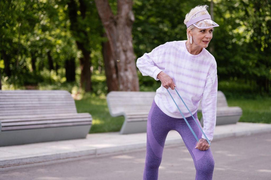 Фітнес-резинки: ефективні вправи для всього тіла Senior woman performing outdoor exercise with a resistance band in a park setting.